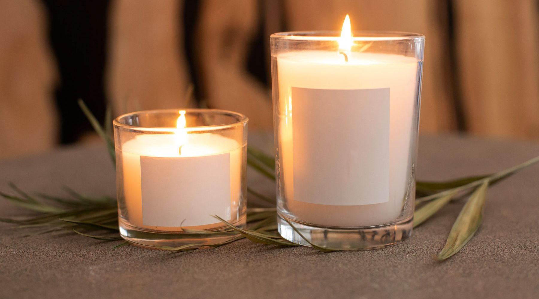 Minimal candles in glass jars with blank labels, surrounded by leaves